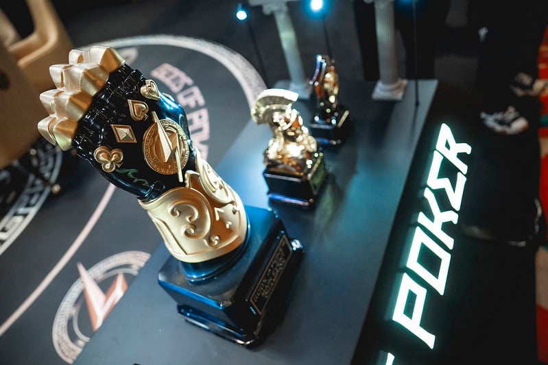 A collection of golden poker trophies, including a fist-shaped one, displayed on a dark table.