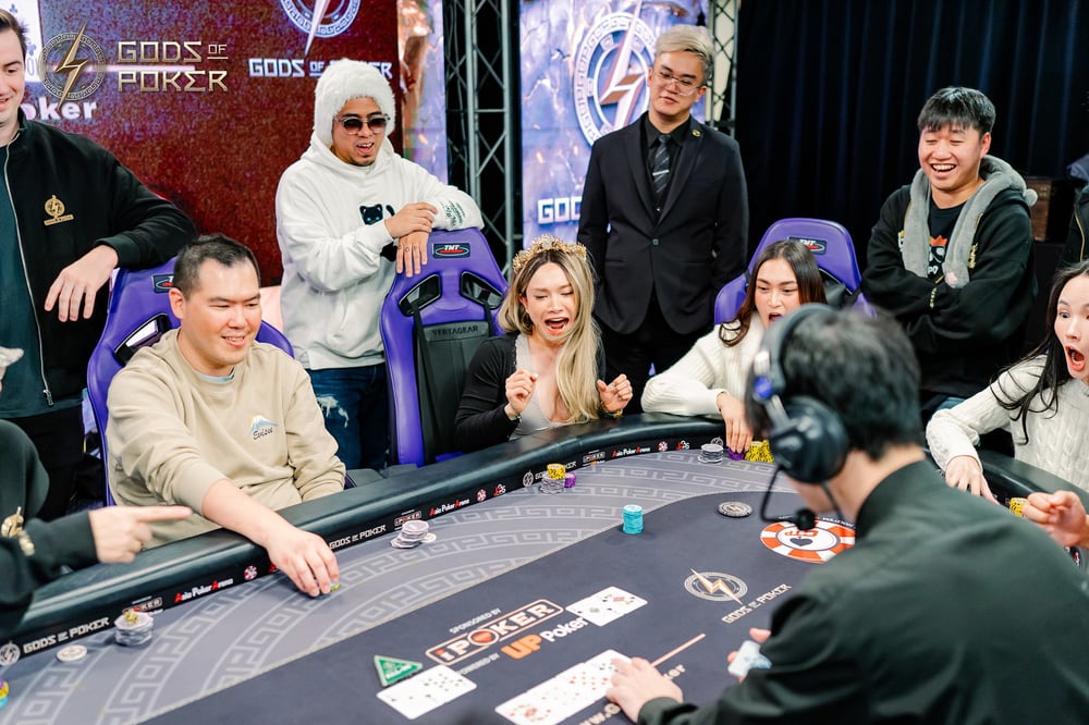People react excitedly around a poker table at a "Gods of Poker" event.