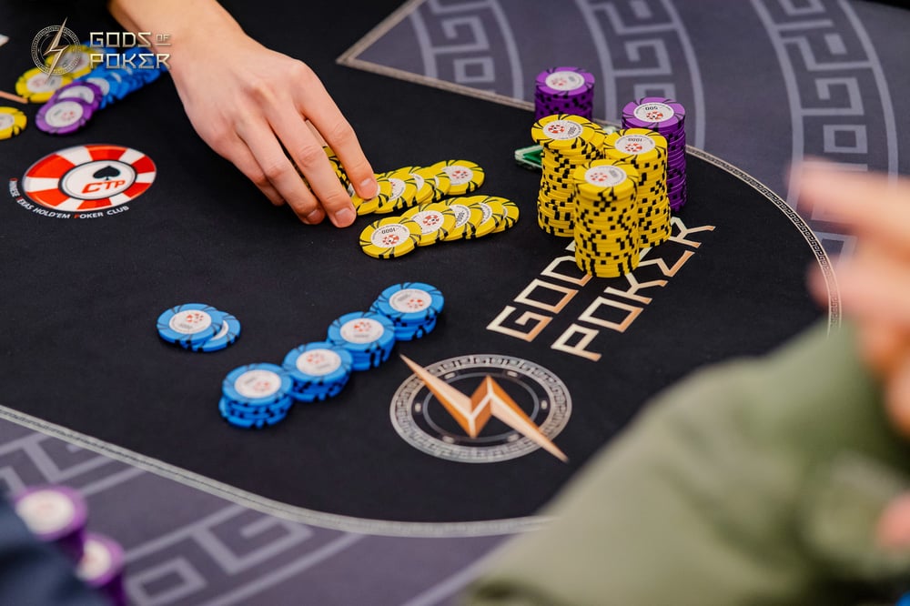 Hands move poker chips across a dark felt table during a high-stakes game.