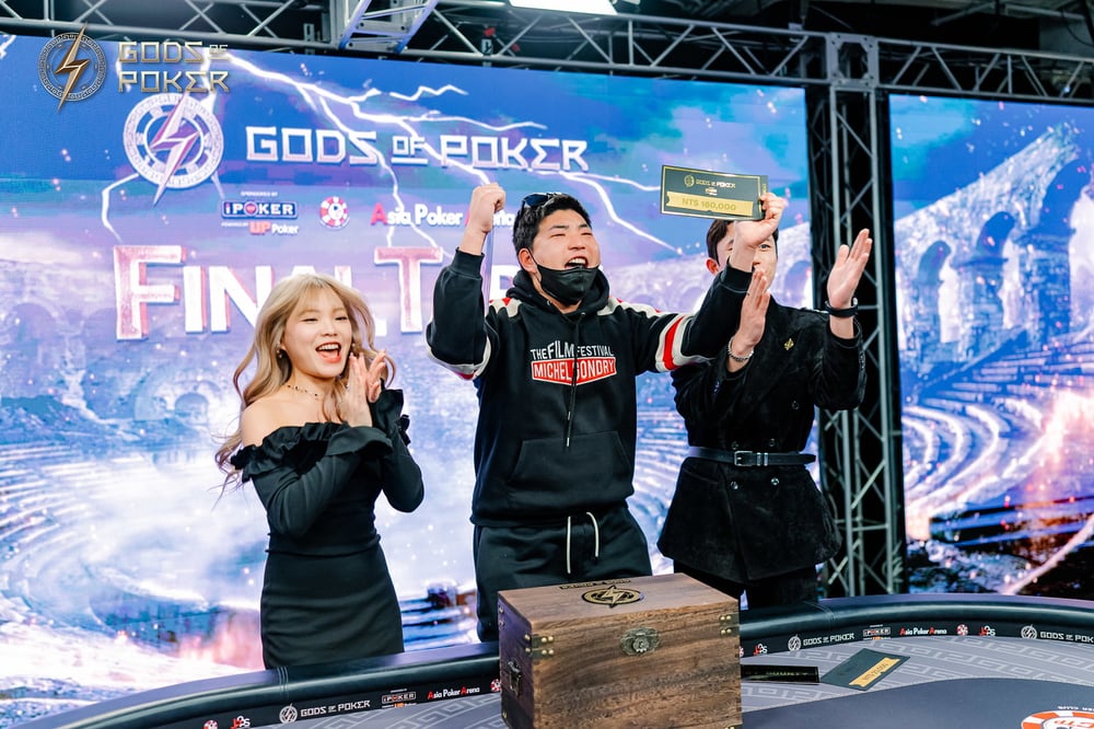 Three people celebrate victory at a Gods of Poker final table event, raising hands.